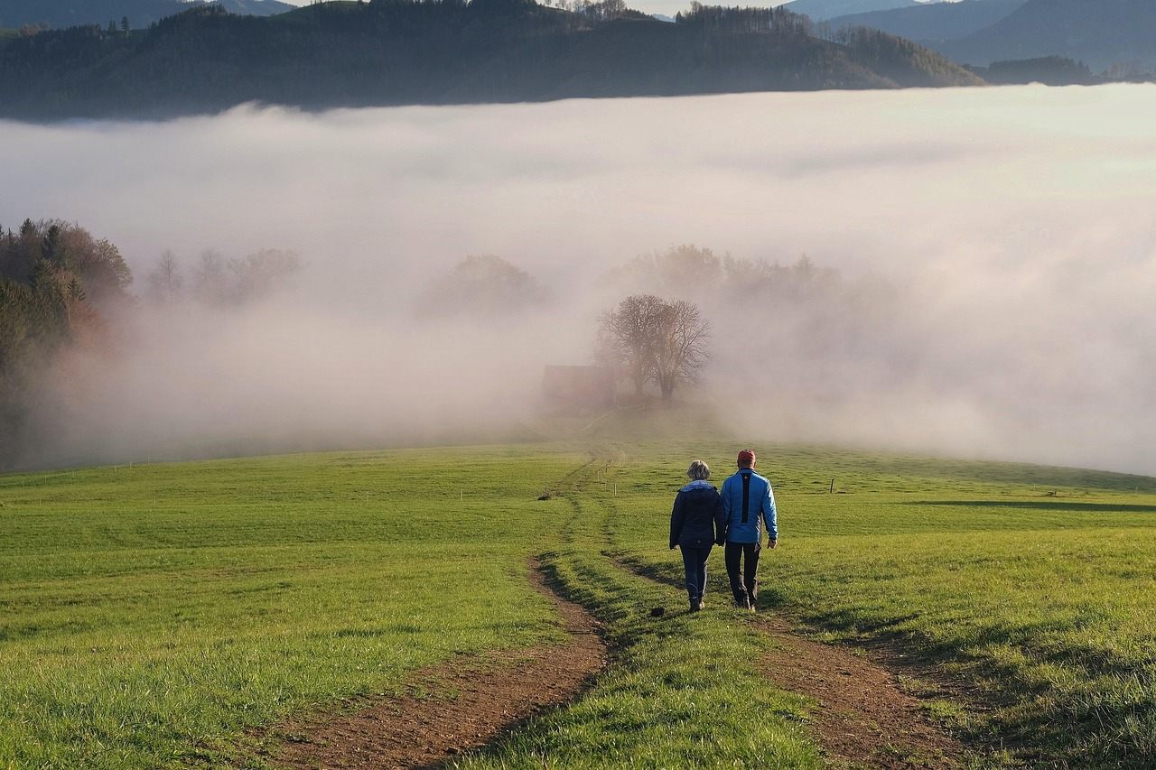 Zwei Menschen gehen gemeinsam einen Weg durch eine neblige Landschaft.
